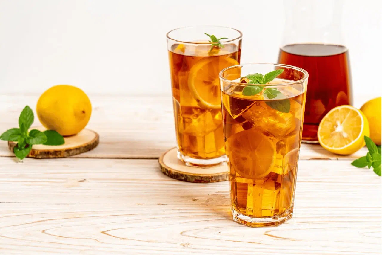 Glasses filled with apple pie moonshine sweet tea next to a pitcher of iced tea