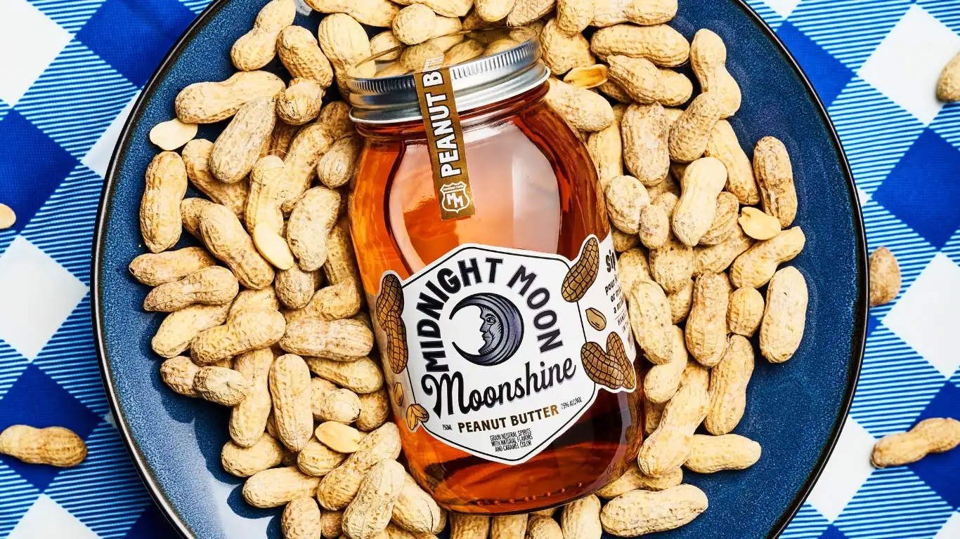 A jar of Midnight Moon Peanut Butter Moonshine in a bowl of peanuts