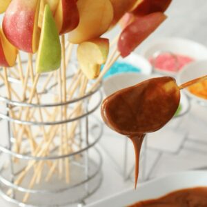 Fresh apple slices being dipped in caramel sauce