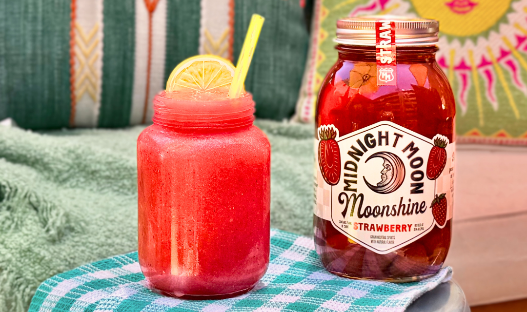 Boozy Strawberry Lemonade Slush with jar of Midnight Moon Strawberry Moonshine on patio
