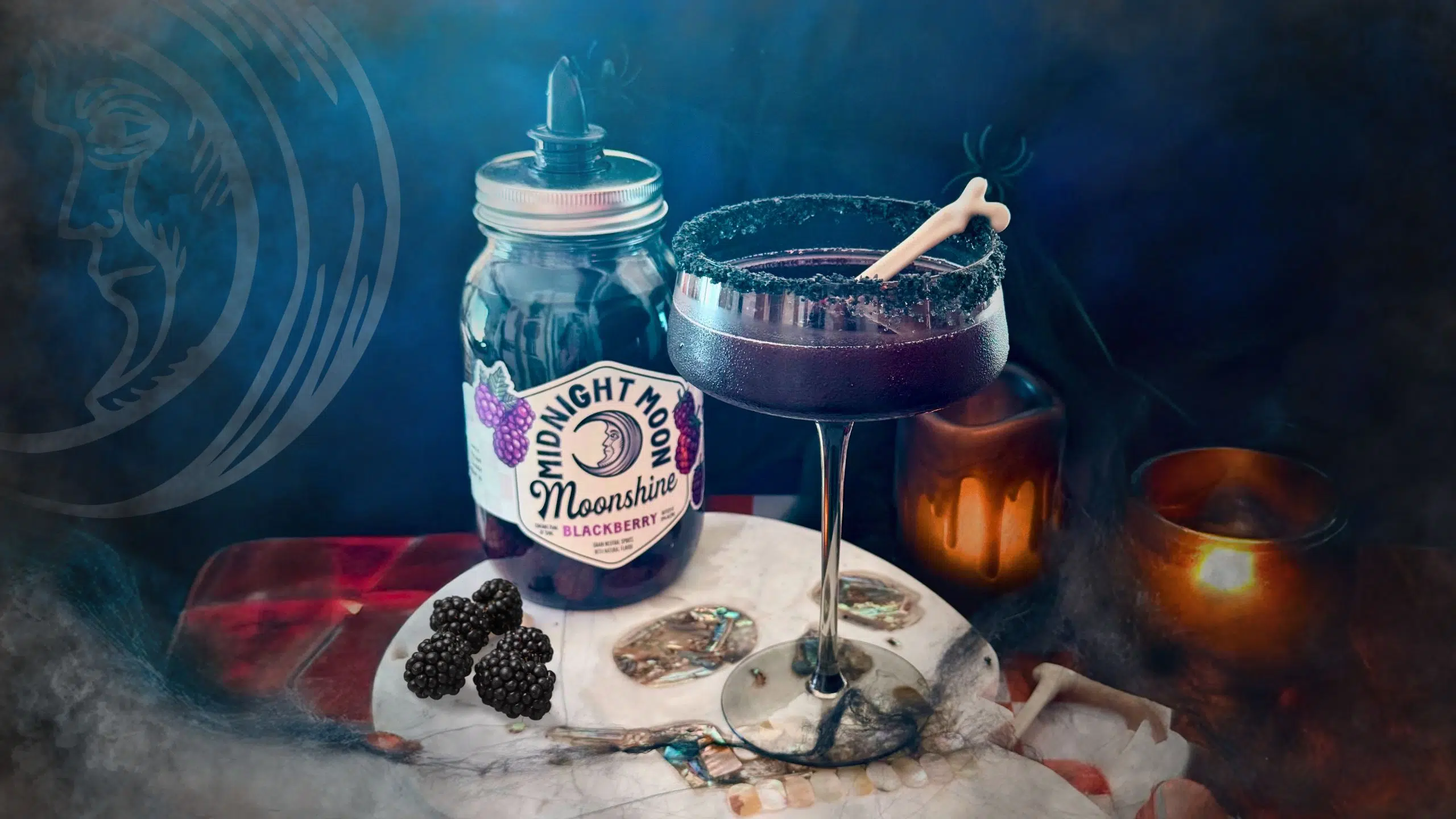 Jar of blackberry moonshine next to a purple cocktail in a black martini glass